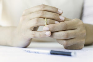 Woman removes wedding ring as she prepares paperwork for her divorce process.