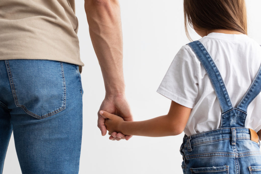 Father and daughter, who are involved in a child custody case, hold hands.